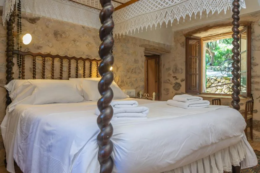 Dormitorio con una gran cama blanca y una ventana abierta con vistas a la vegetación.