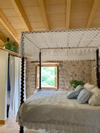 Un dormitorio con cama con dosel, paredes de piedra y una ventana con vistas a la vegetación.