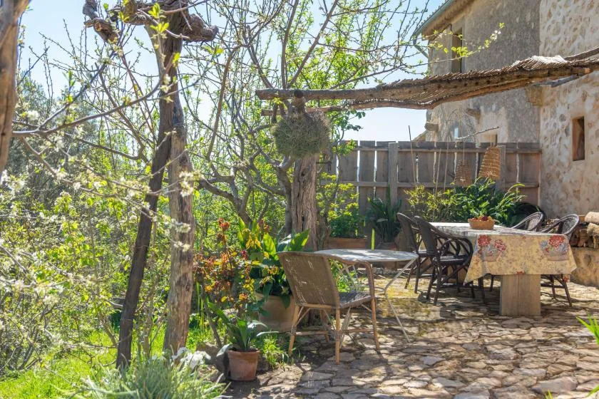 Un patio exterior de piedra con una mesa, asientos y árboles alrededor.
