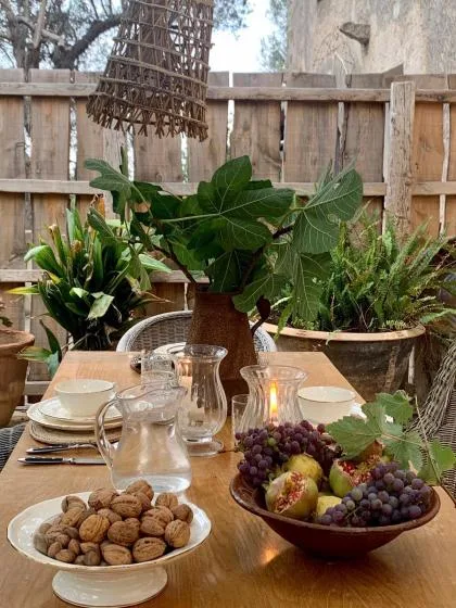 Una mesa de comedor al aire libre está puesta con platos, fruta y plantas frondosas.