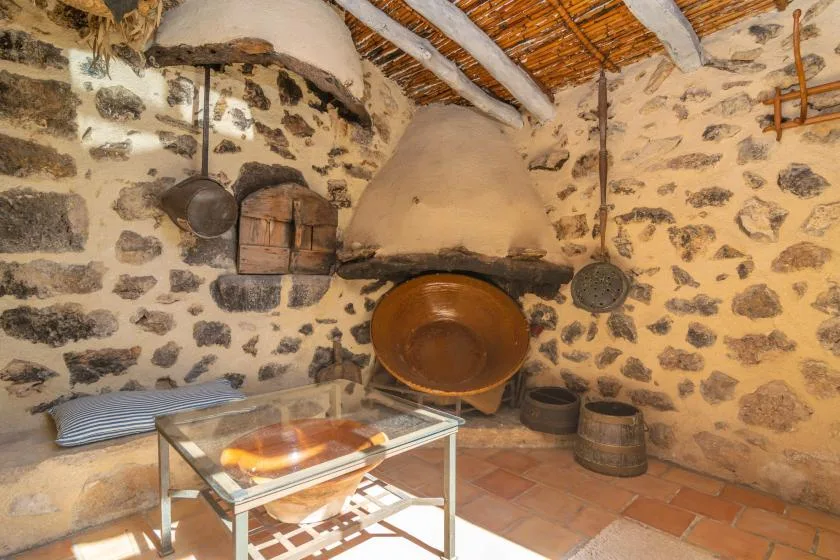 Una cocina rústica de piedra con una gran chimenea y una mesa de exhibición de vidrio.