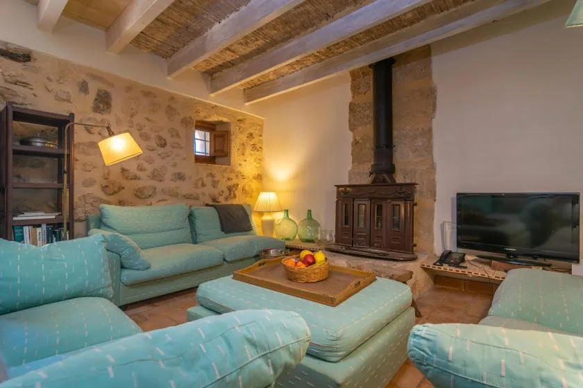 Una sala de estar con asientos turquesa, una estufa de leña y un televisor.