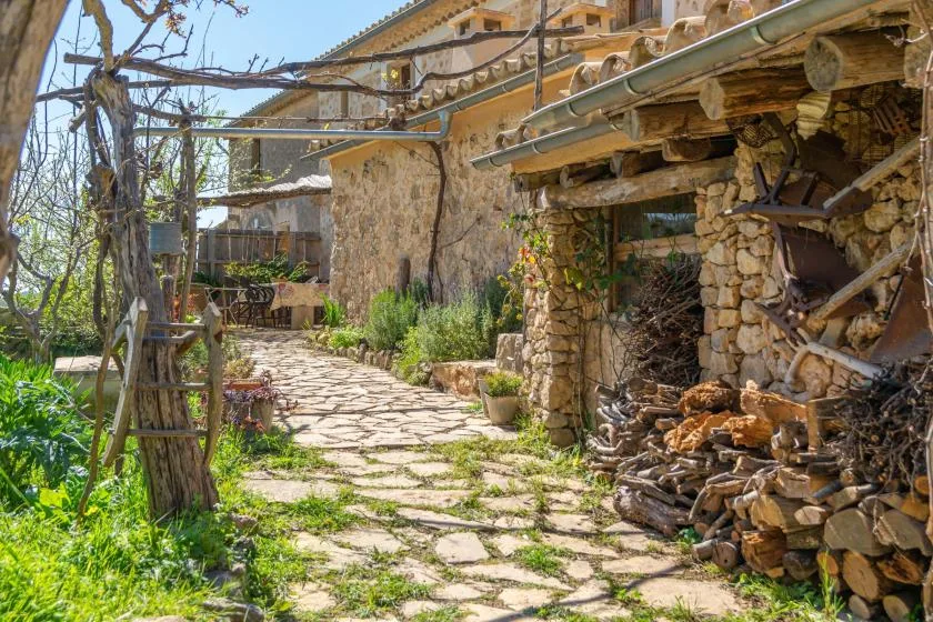 Un sendero de piedra atraviesa un patio junto a un edificio de piedra y leña apilada.