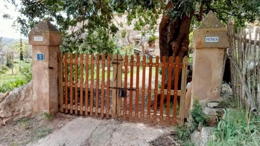 A wooden gate between stone pillars opens onto a leafy outdoor path.