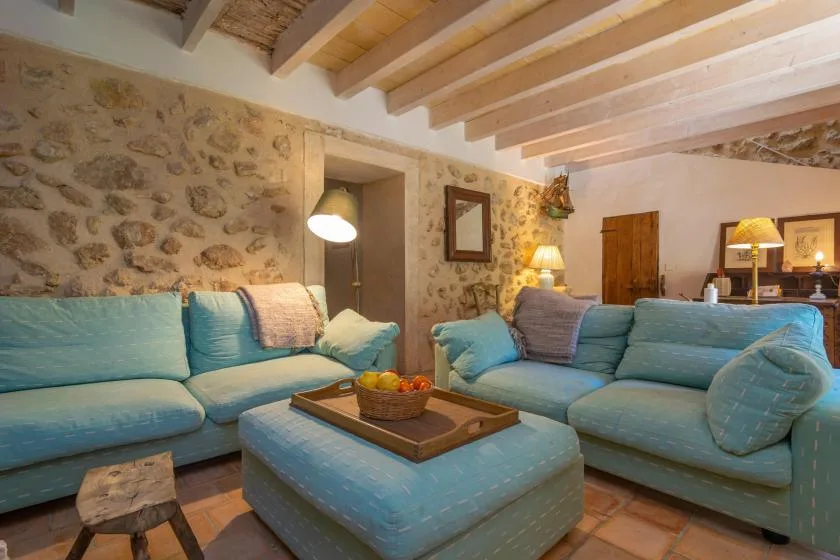 Una sala de estar con asientos azules, un reposapiés a juego y vigas de madera a la vista.