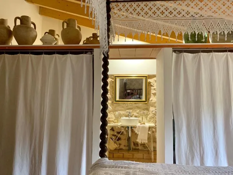 Un espacio para dormir con cortinas da a un baño de piedra con lavabo.