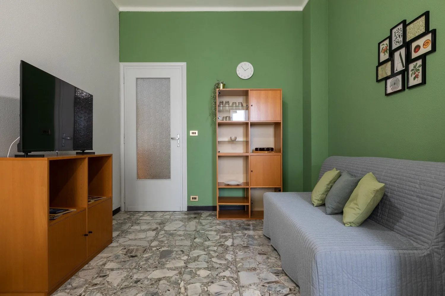 A living room with a television, shelving unit, and seating against green walls.