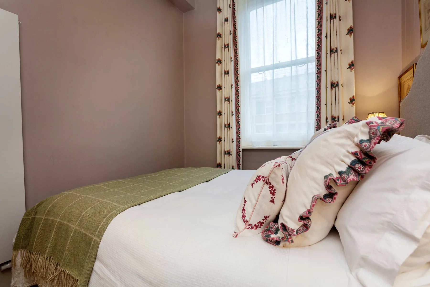 Un dormitorio con una cama, almohadas estampadas y una ventana con cortinas.