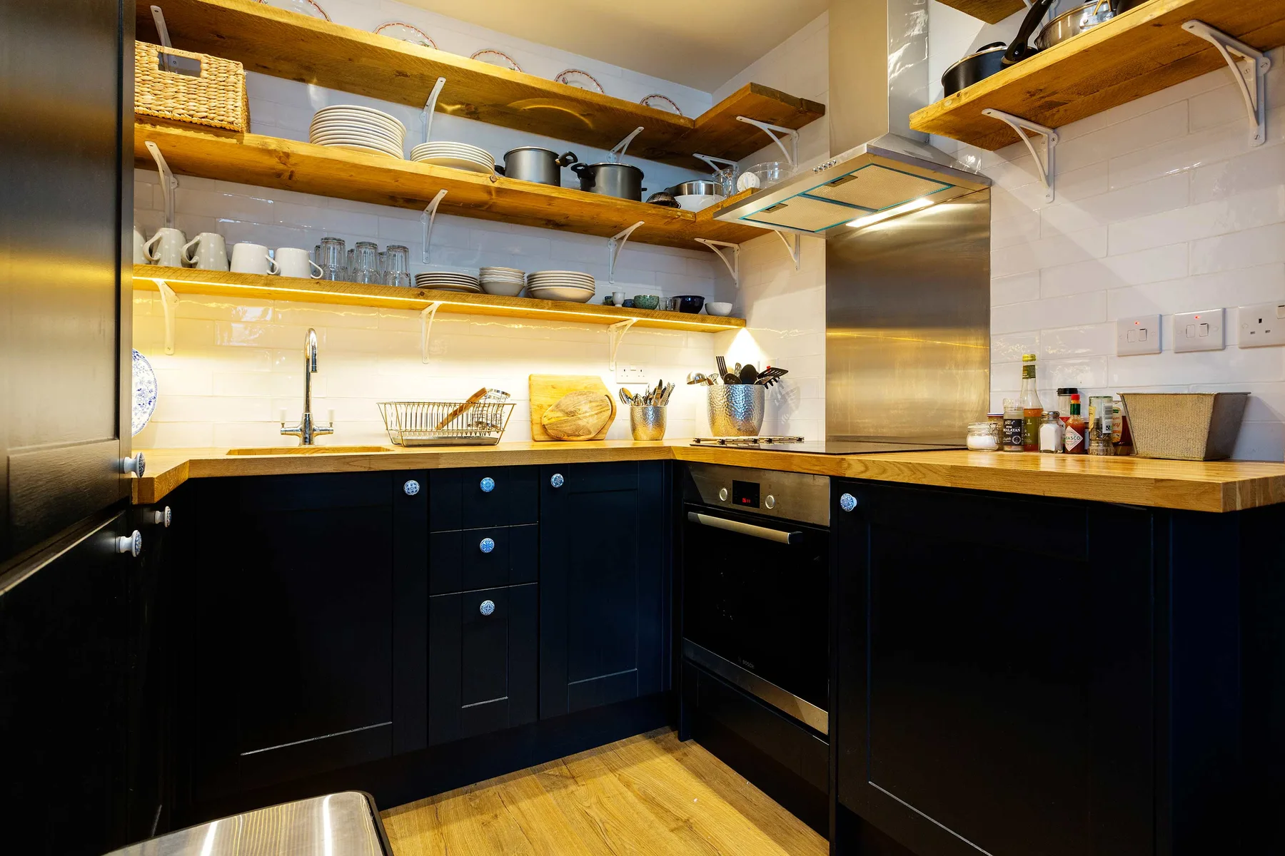 Una cocina con gabinetes oscuros, encimeras de madera y estantes abiertos con platos.