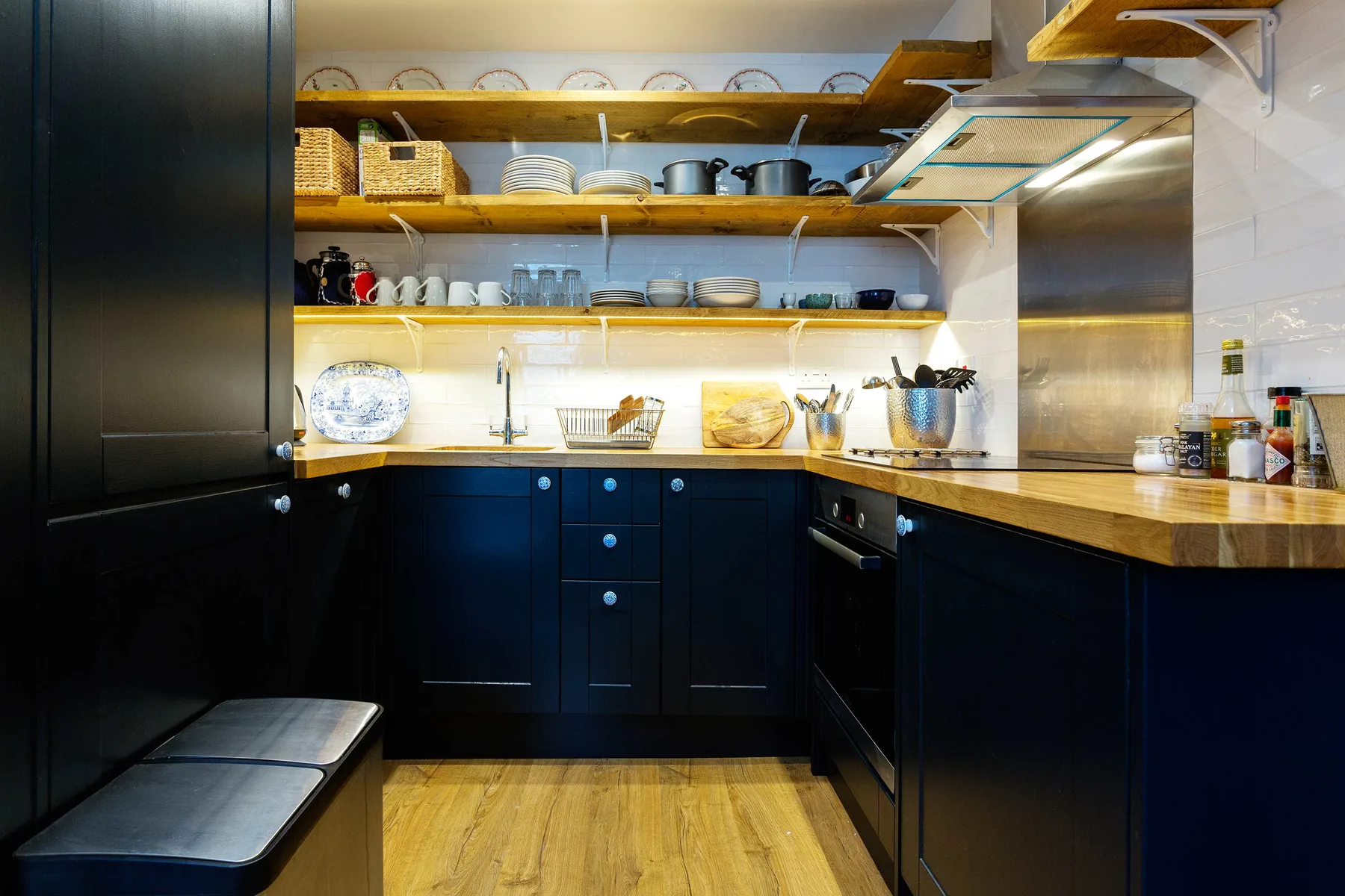 Una cocina con gabinetes oscuros, estantes abiertos y piso de madera.