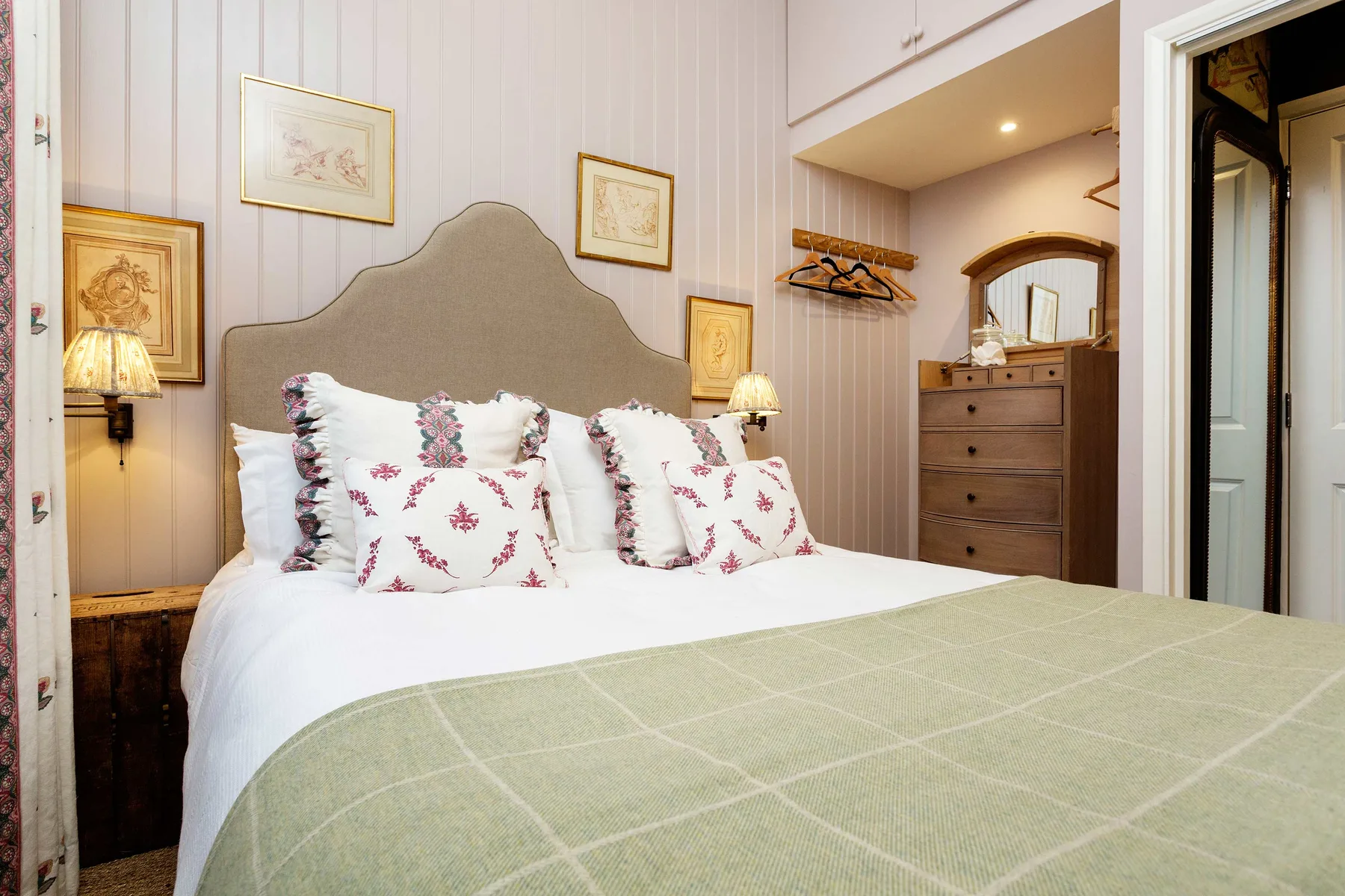 Un dormitorio con una cama bien hecha, cojines estampados y una cómoda.