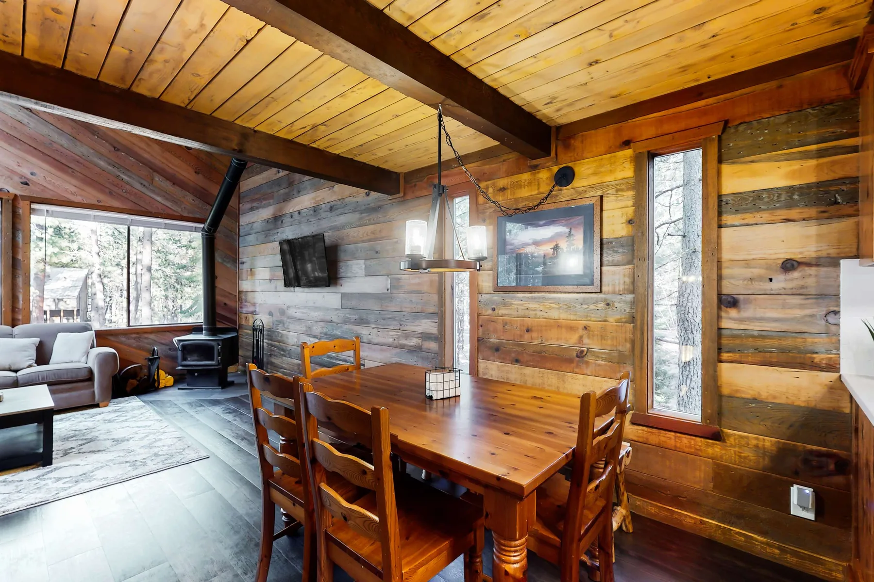 Una sala y comedor revestidos de madera, con mesa, asientos y ventanales.