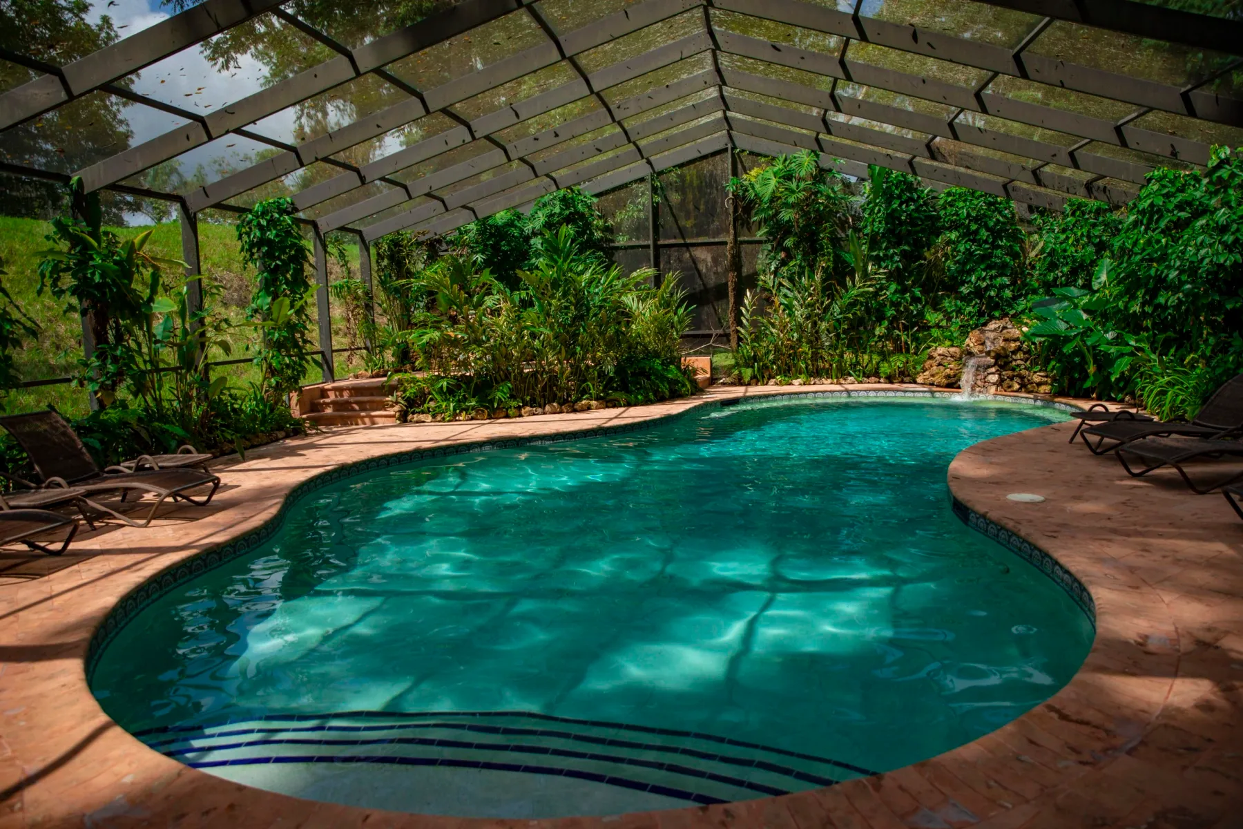 Piscina con cerramiento de malla y tumbonas en la terraza