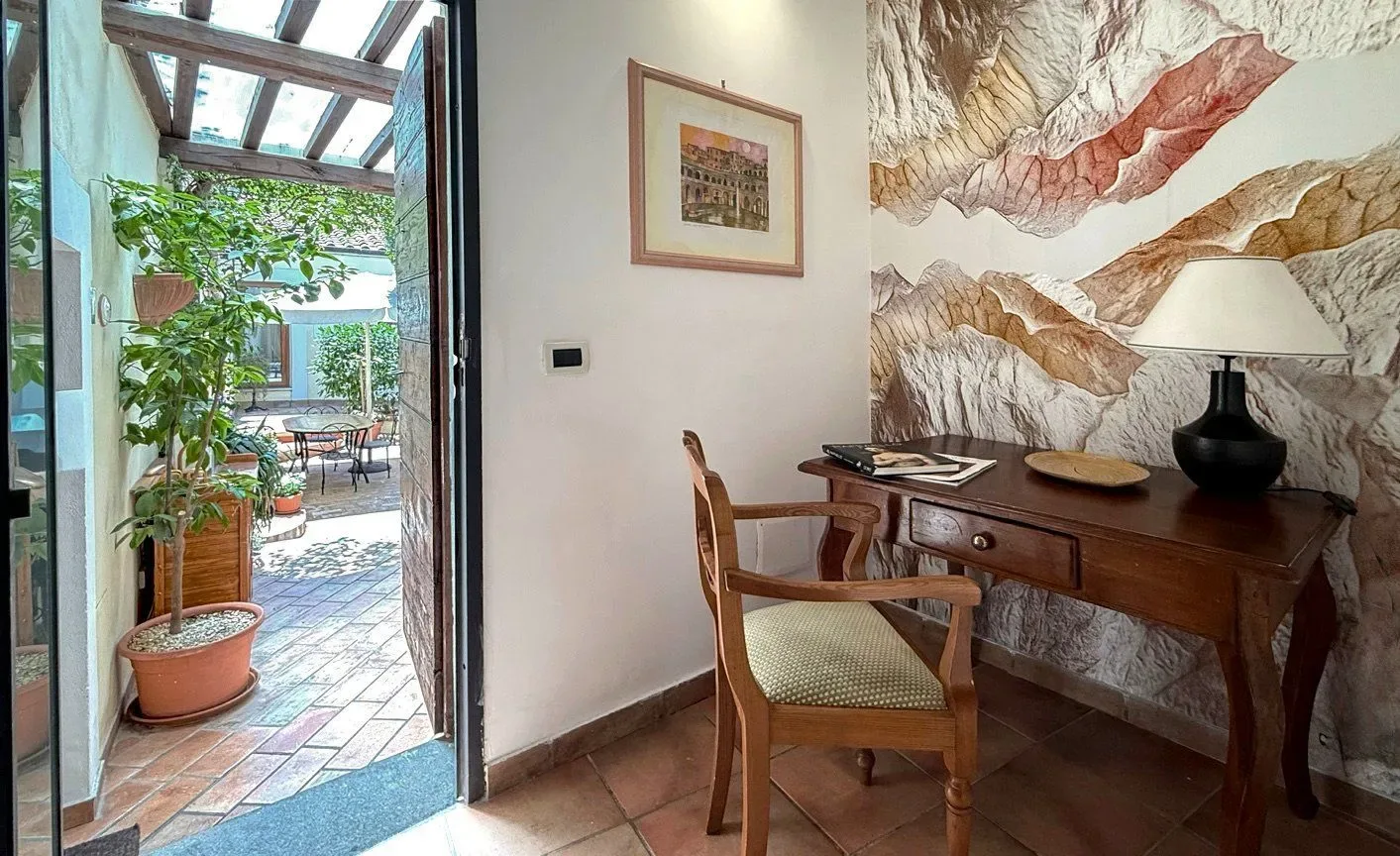Interior con escritorio, silla, puerta abierta al patio y arte en la pared.