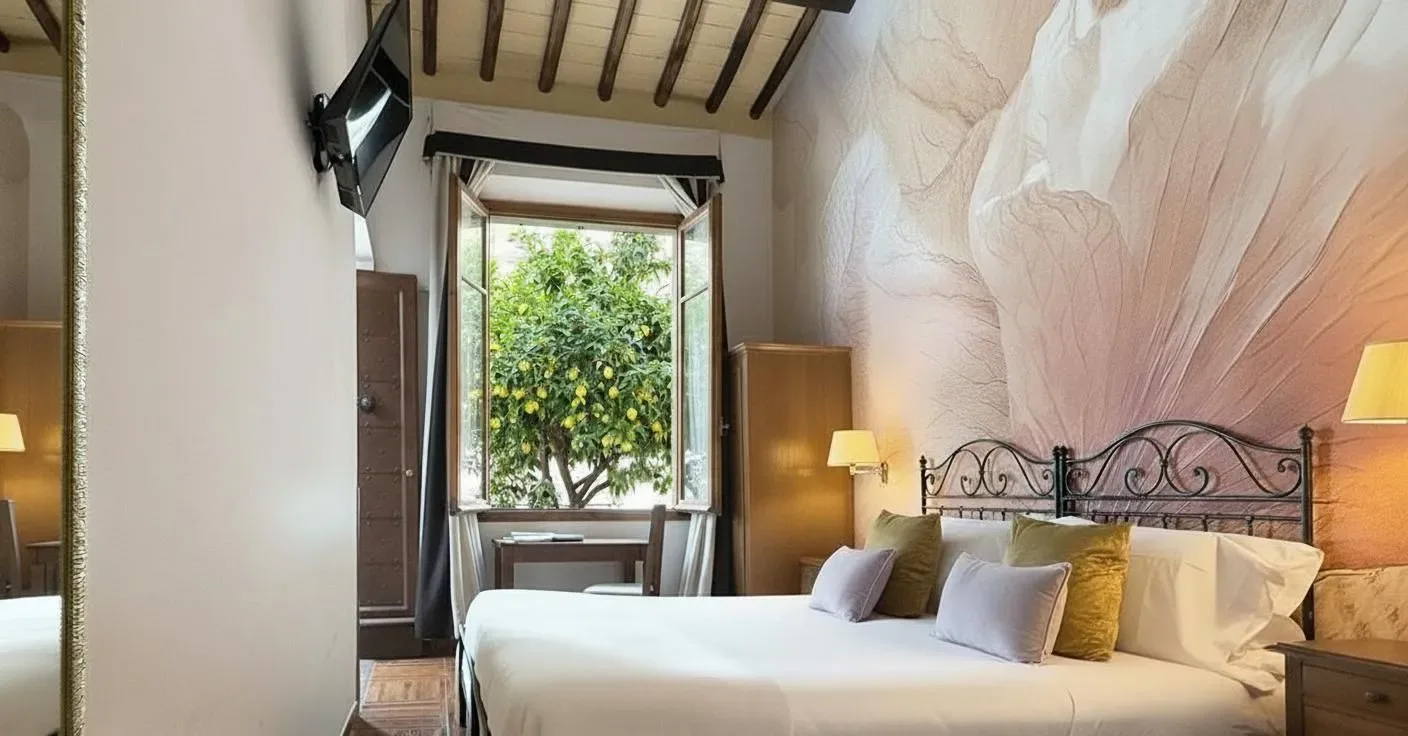 Dormitorio con cama, papel pintado floral y ventana con vistas a un árbol.