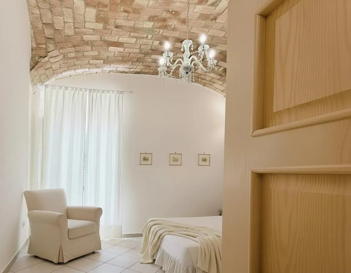 Dormitorio con techo abovedado de ladrillo, paredes blancas y sillón.