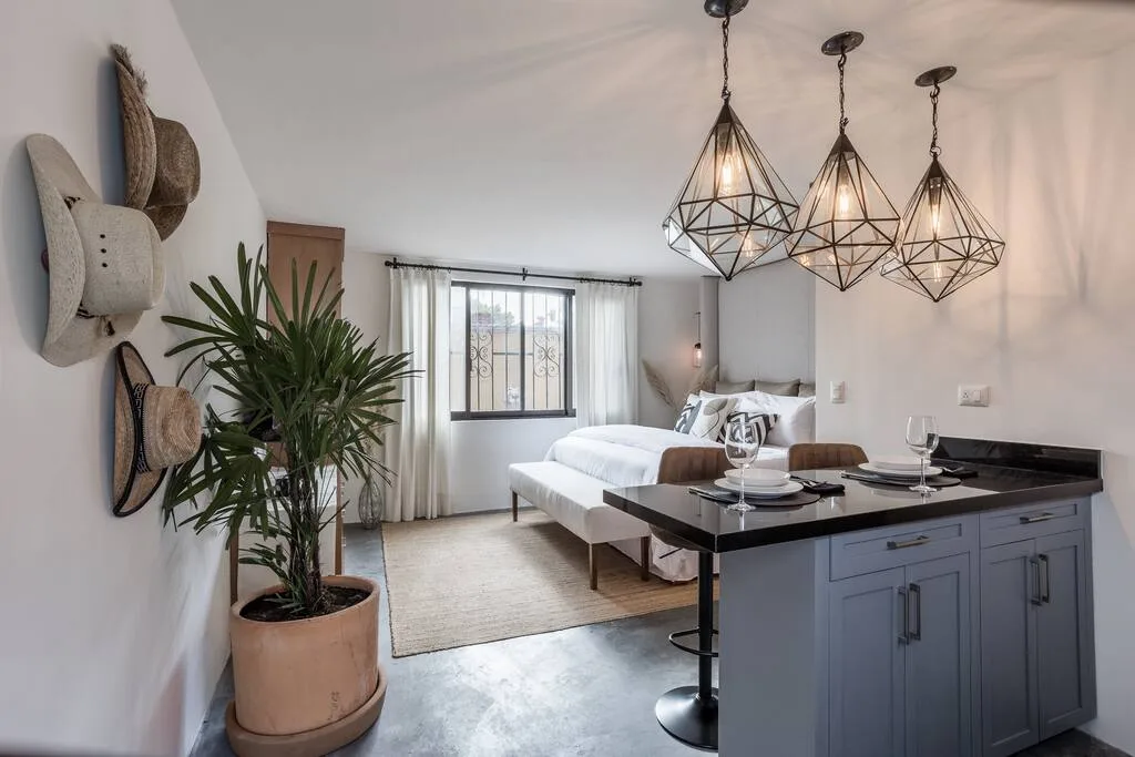 A bedroom with a bed and a kitchen island beneath geometric pendant lights.