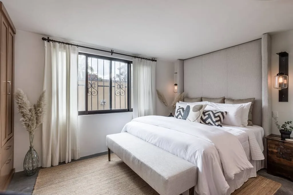 Bedroom with king bed, large window with sheer curtains, and pendant lighting