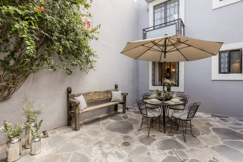 Courtyard with dining table under umbrella, wooden bench, and climbing vines on walls