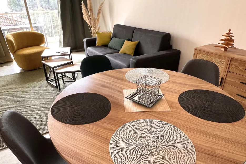 A living room with a dark sofa, armchair, and round wooden dining table.