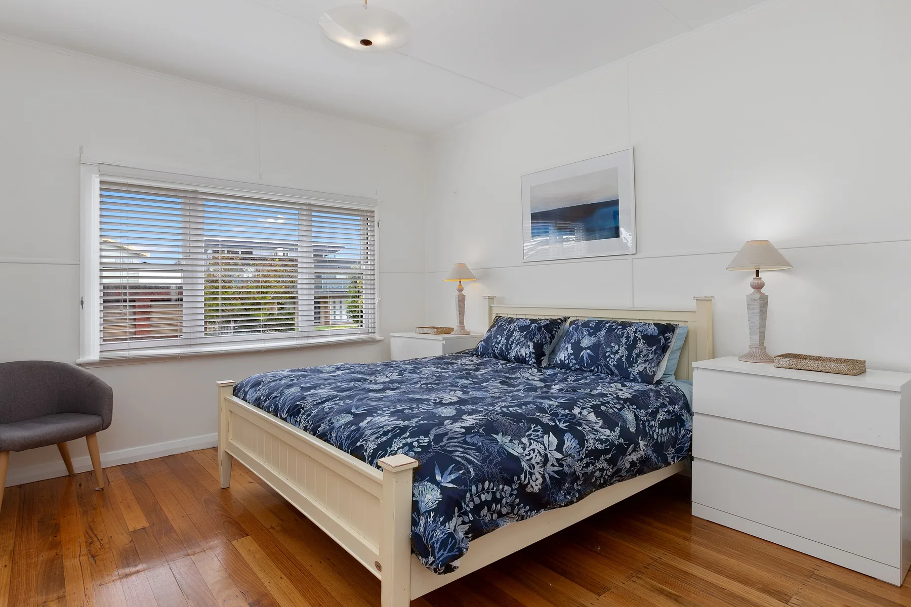 Un dormitorio luminoso tiene una cama con ropa de cama azul estampada y una ventana con persianas.
