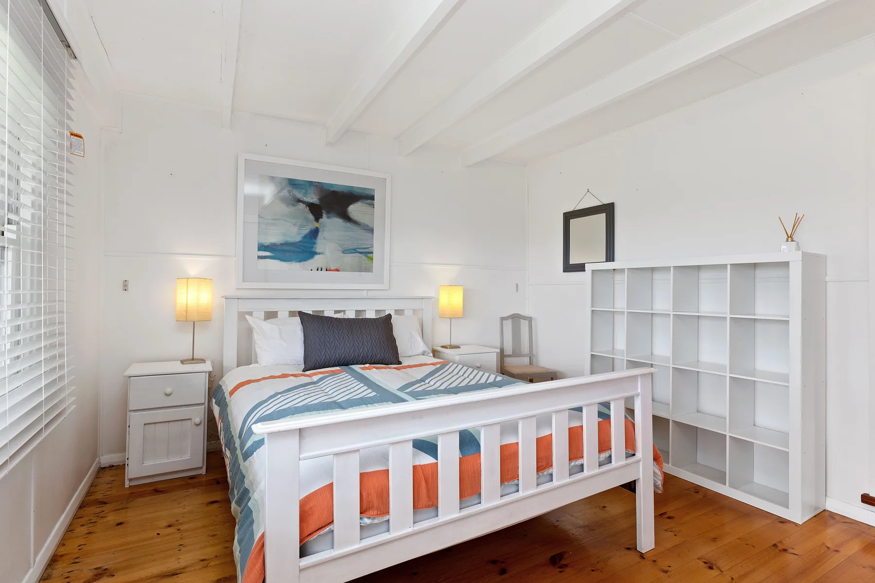 Un dormitorio luminoso con una cama, lámparas de noche y estanterías blancas.