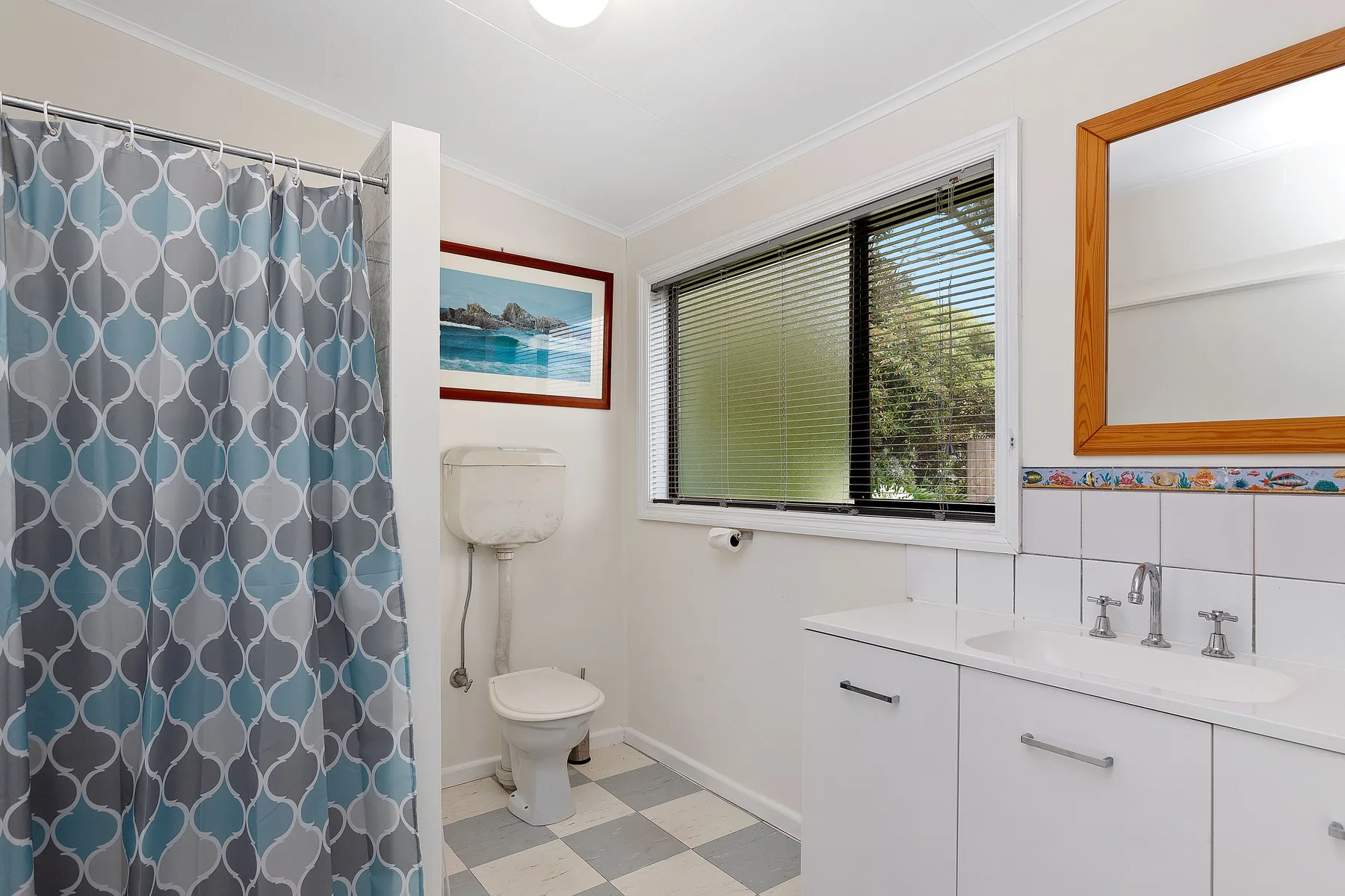 Un baño con una cortina de ducha estampada, inodoro y lavabo junto a una ventana.