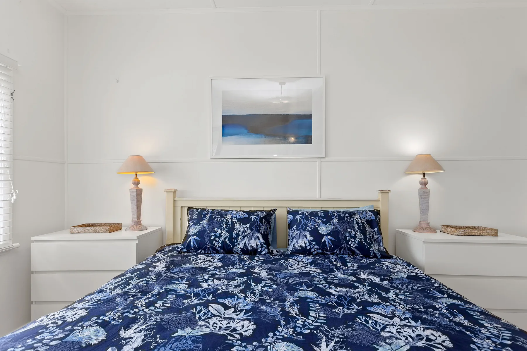Un dormitorio con una cama vestida con ropa de cama floral azul y mesitas a los lados.