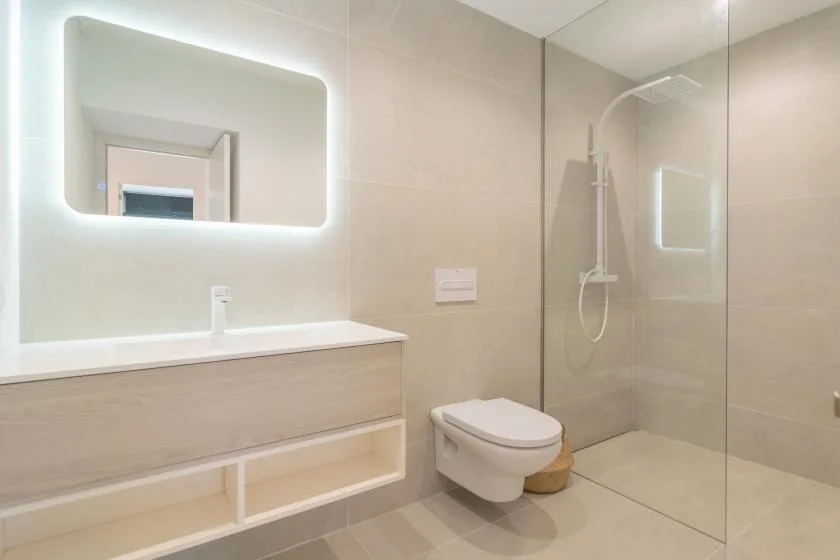 A modern bathroom with a vanity, wall mirror, toilet, and shower.