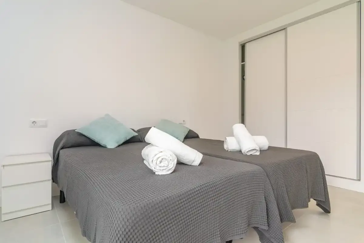 A bedroom with two beds, gray bedding, and folded white towels.