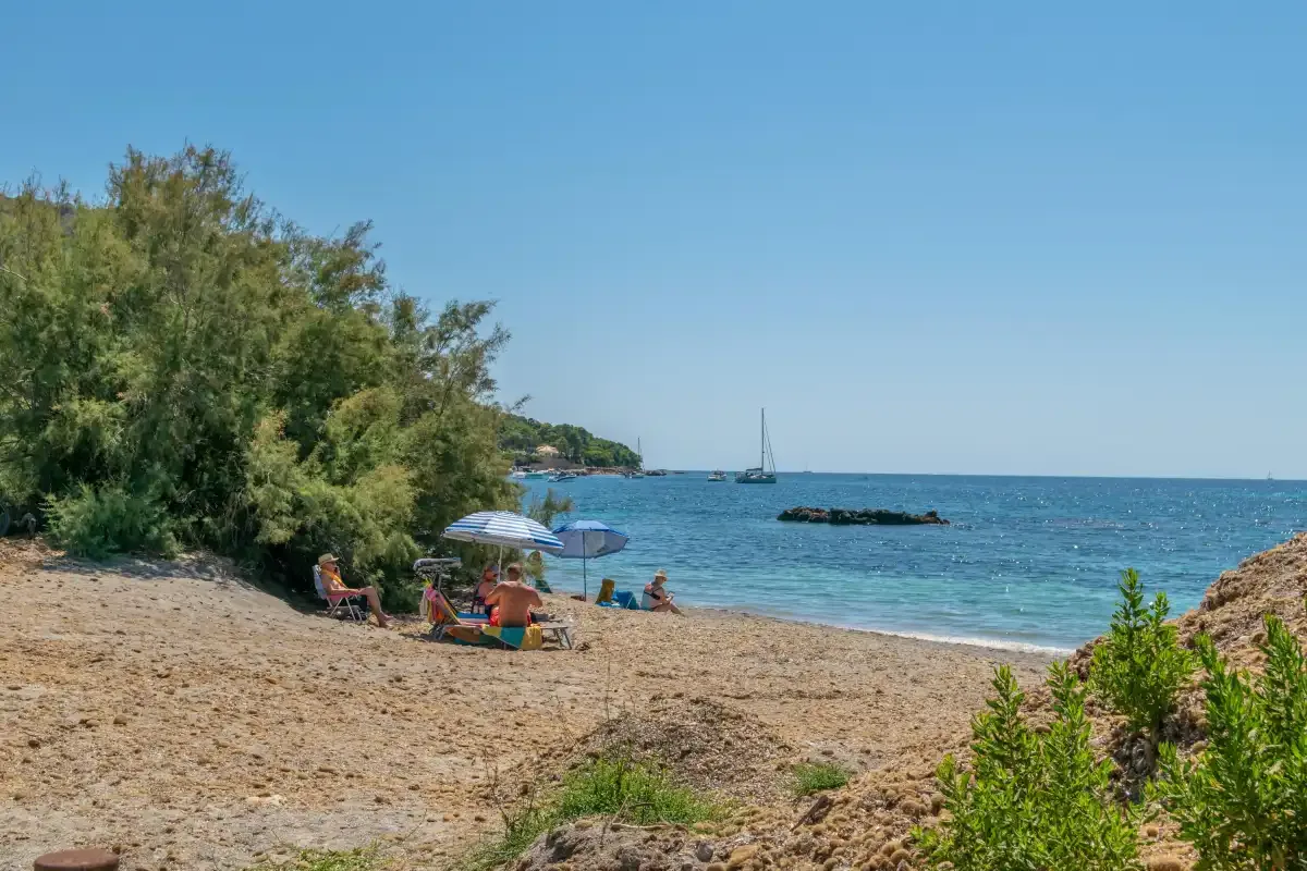 A sandy beach with people under umbrellas beside the blue sea.