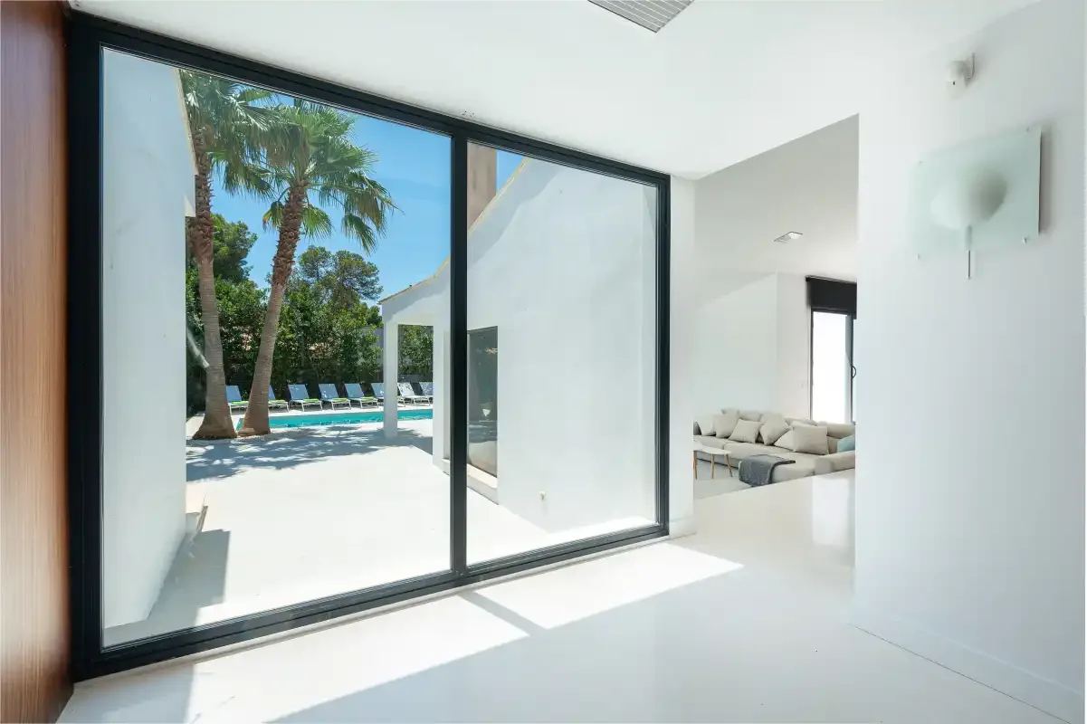 A bright interior opens through large glass doors to a pool and palm trees.
