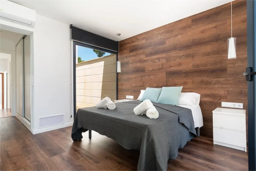 A bedroom with a bed against a wood-paneled wall and a window.