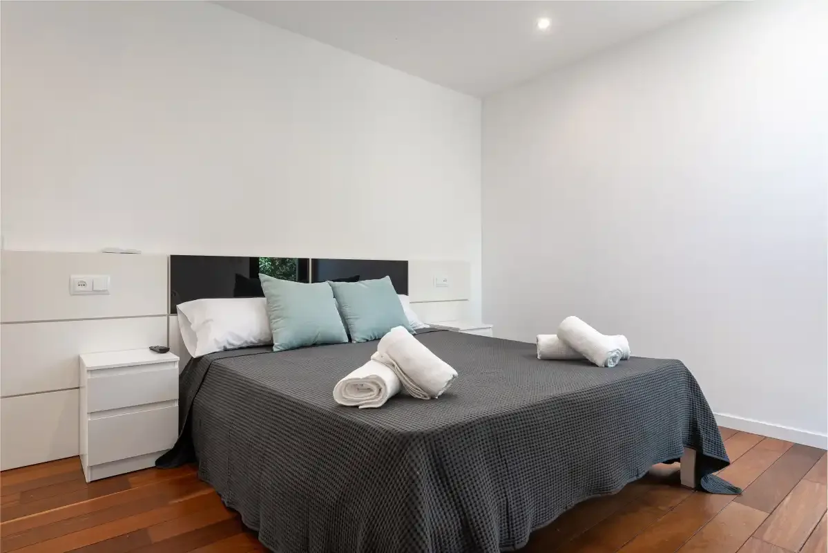 A bedroom with a dark bedspread and pale pillows.