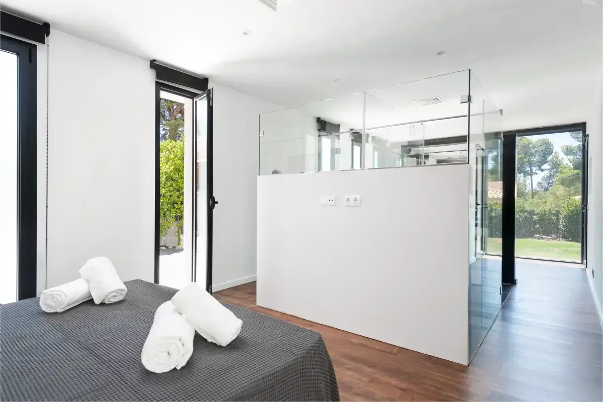 A bright bedroom with a bed beside a glass-enclosed shower area.
