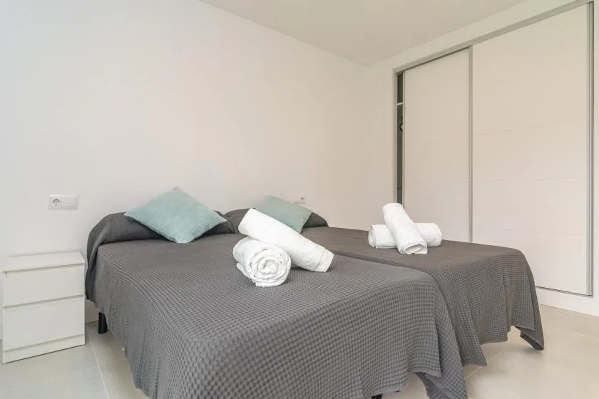 A bedroom with two beds covered in gray bedspreads and folded towels.