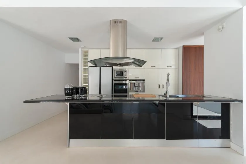 A modern kitchen with a glossy dark island and stainless steel range hood.