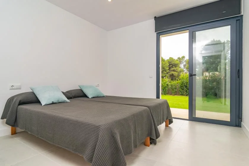 A bedroom with a double bed and sliding glass doors opening onto a green garden.