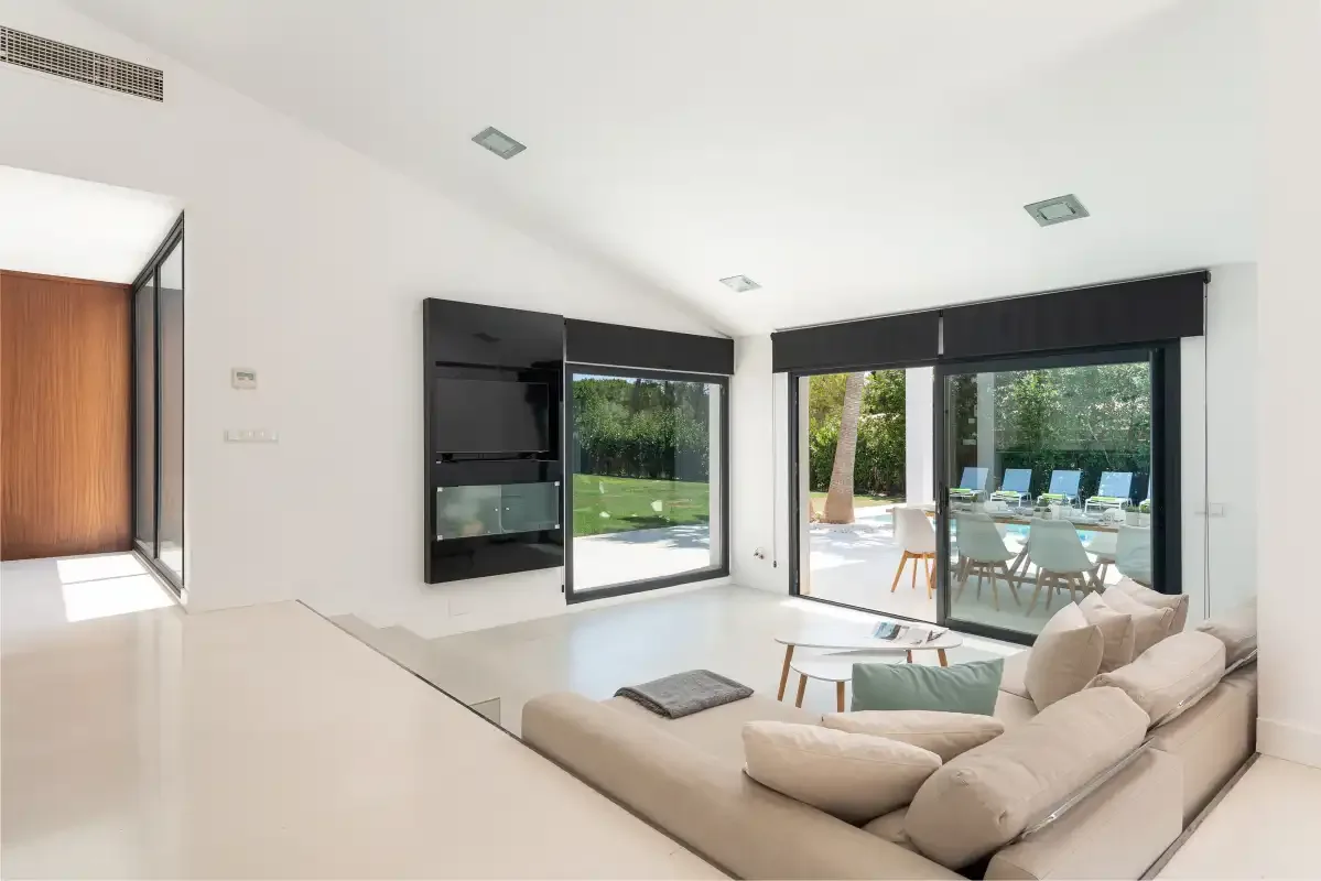 A bright living room with seating beside large windows opening onto a patio.