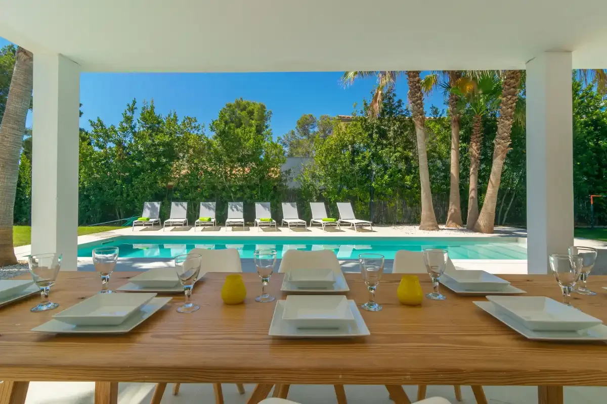 A dining table overlooks an outdoor swimming pool surrounded by greenery.