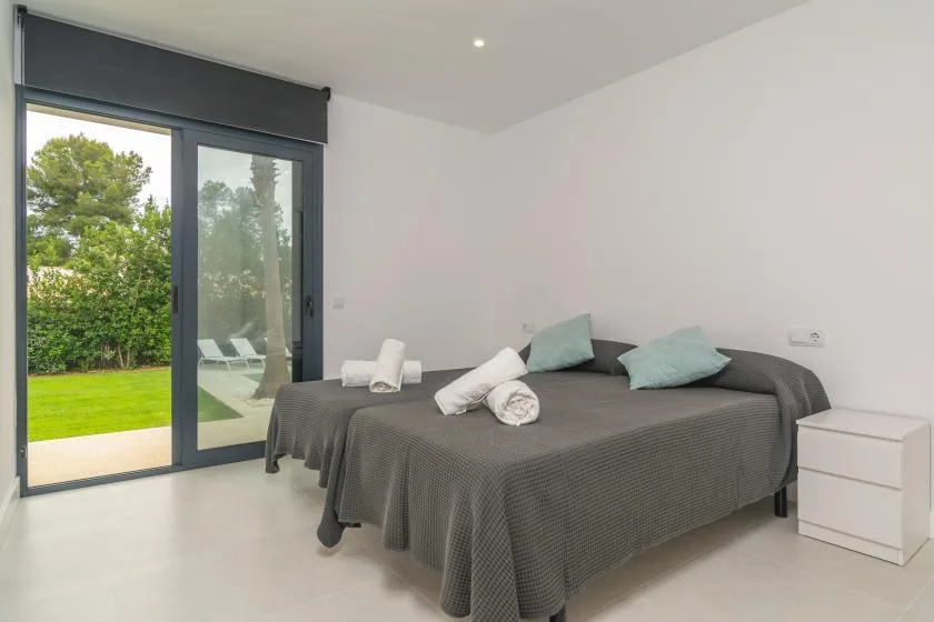 A bedroom with a bed, pale pillows, and a large glass door overlooking greenery.