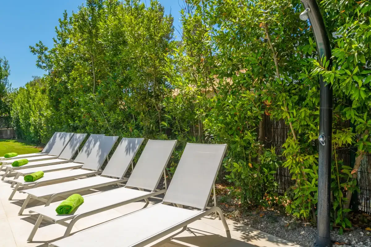 Outdoor seating lines a sunny patio beside a lush green hedge.