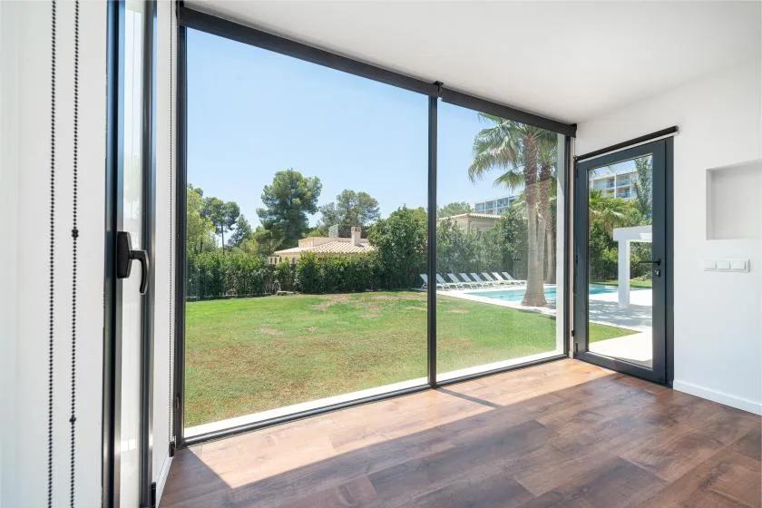 A bright room opens onto a lawn and swimming pool through large glass doors.