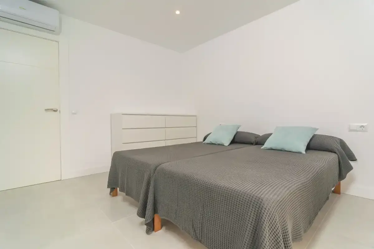 A bright bedroom with a large bed dressed in gray bedding and pale blue pillows.