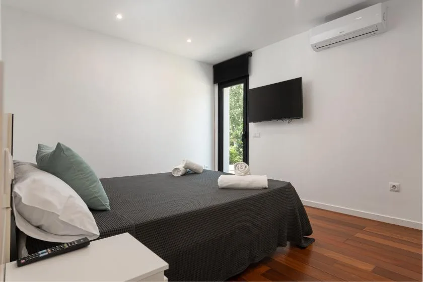 A bedroom with a dark bedspread, wall-mounted television, and air conditioner.