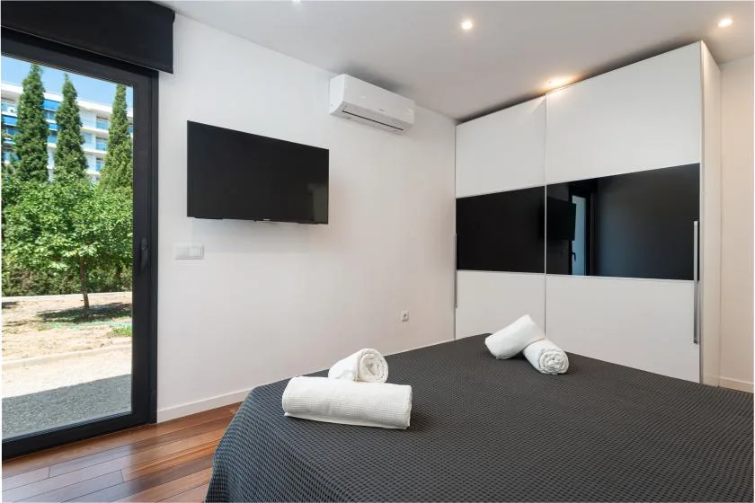 A bedroom with a neatly made bed, wall-mounted television, and large window.