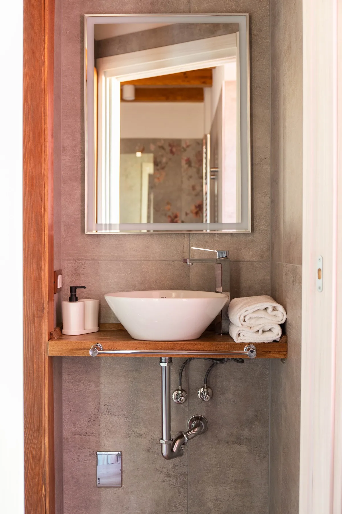 Un lavabo de baño con una cuenca blanca, un espejo de pared y tuberías visibles.