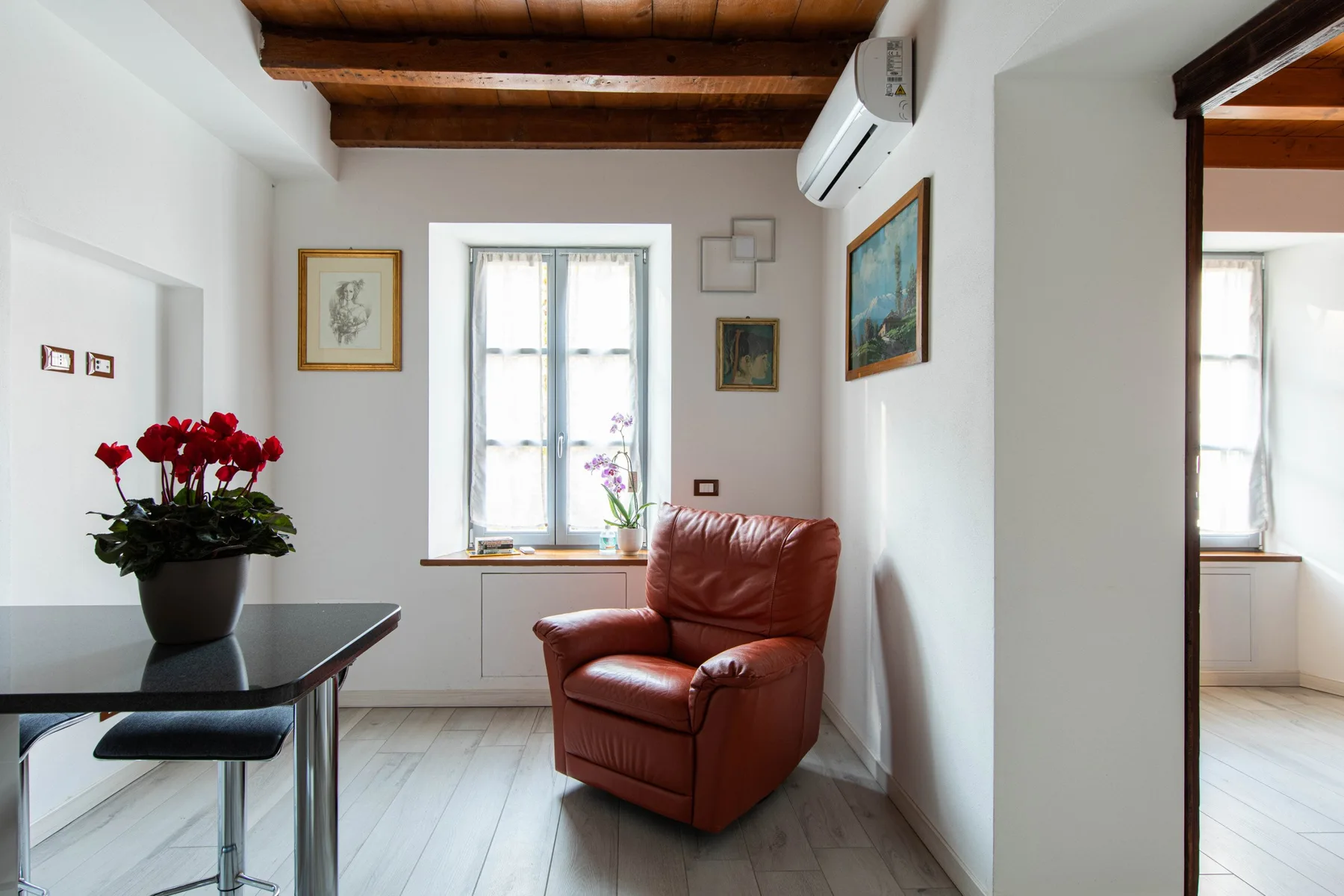 Una pequeña zona de estar con un sillón marrón junto a una ventana luminosa.