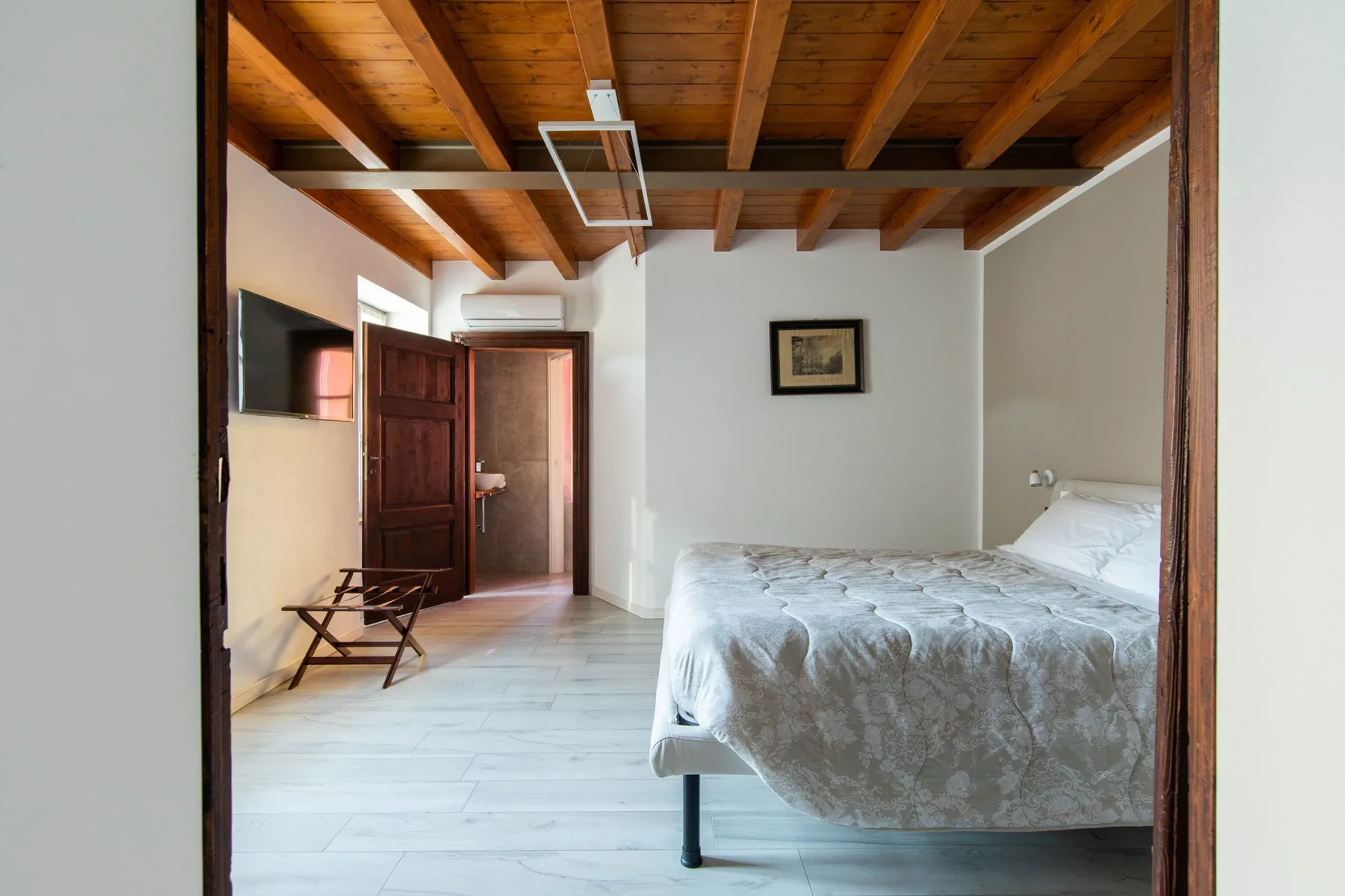 Un dormitorio con una cama, un televisor en la pared y vigas de madera a la vista.