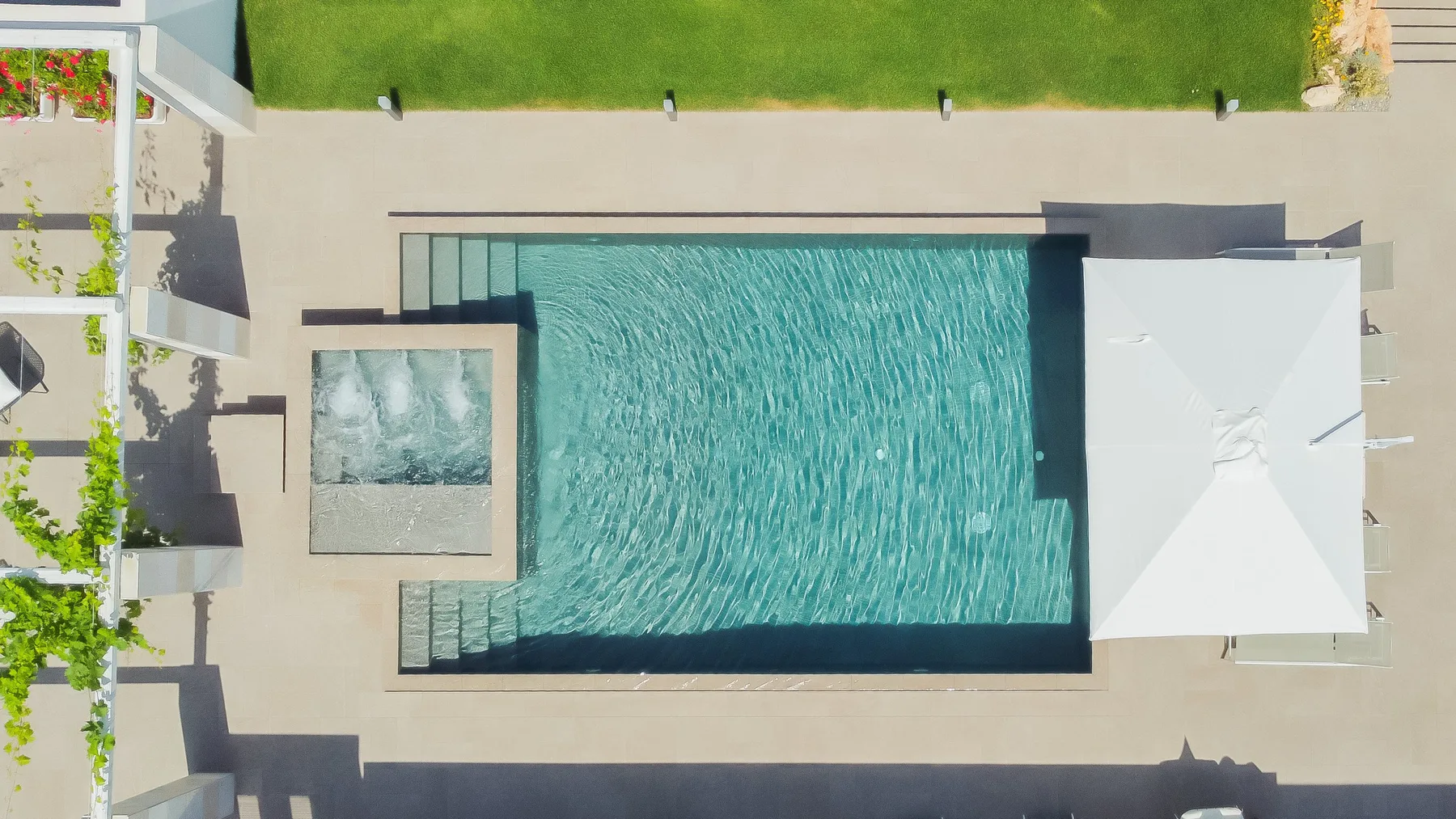 Una piscina al aire libre está junto a una terraza pavimentada y una sombrilla blanca.